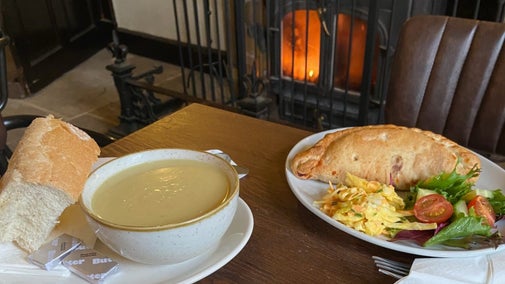 A bowl of soup and a pasty with salad garnish on a table in front of a fire at Grantham House.